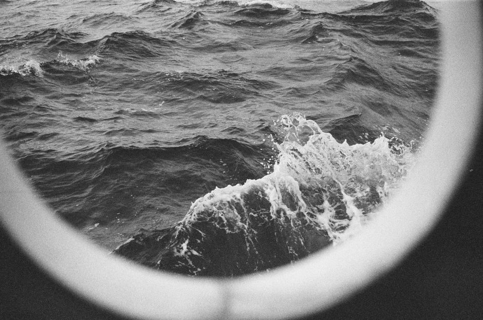 Artistic view of ocean waves through a ship's porthole in monochrome.