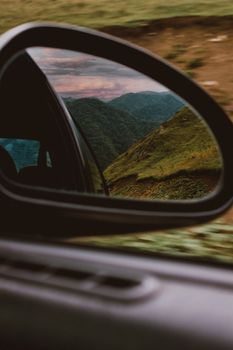 Beautiful view of lush green mountains reflected in a car side mirror during a scenic drive.
