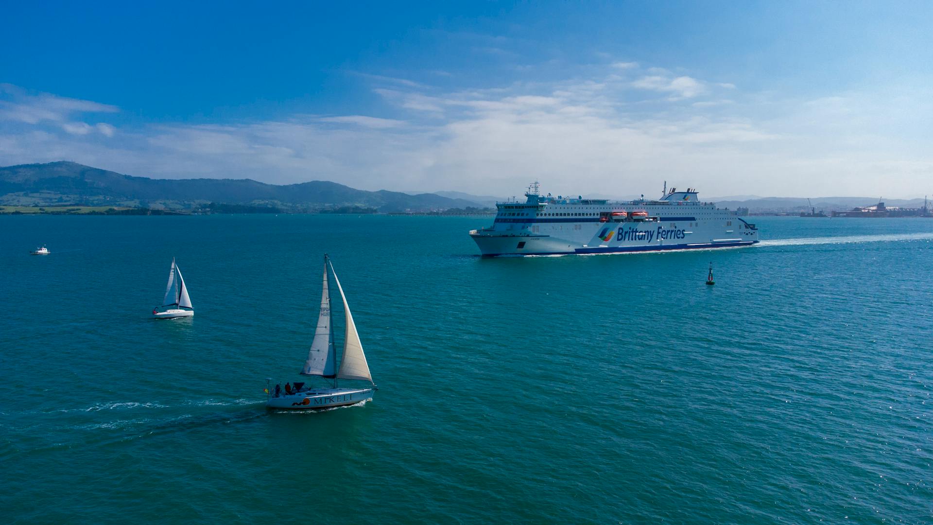 A ferry and sailboats navigate the tranquil waters of Santander Bay under a clear blue sky.