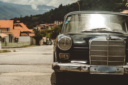 Free Classic Mercedes Benz parked on a vibrant street in Venezuela with mountain backdrop. Stock Photo