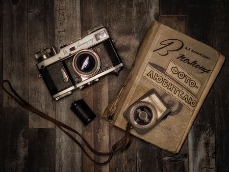 Flatlay of vintage camera, light meter, and photo book on wooden surface.