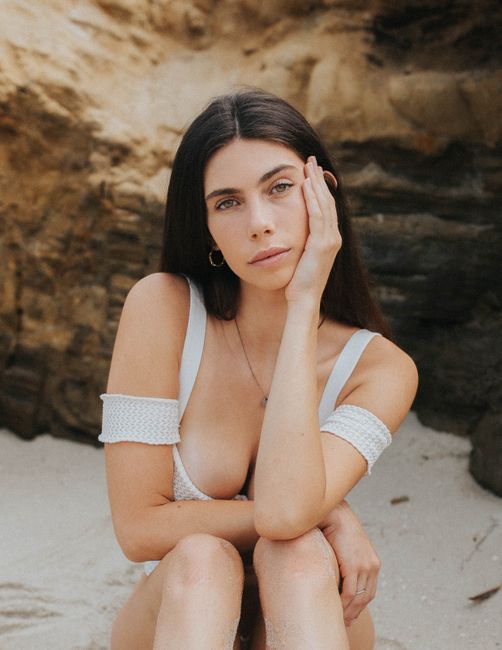 Portrait of a woman in white bikini sitting on a sandy beach, exuding calmness and beauty.