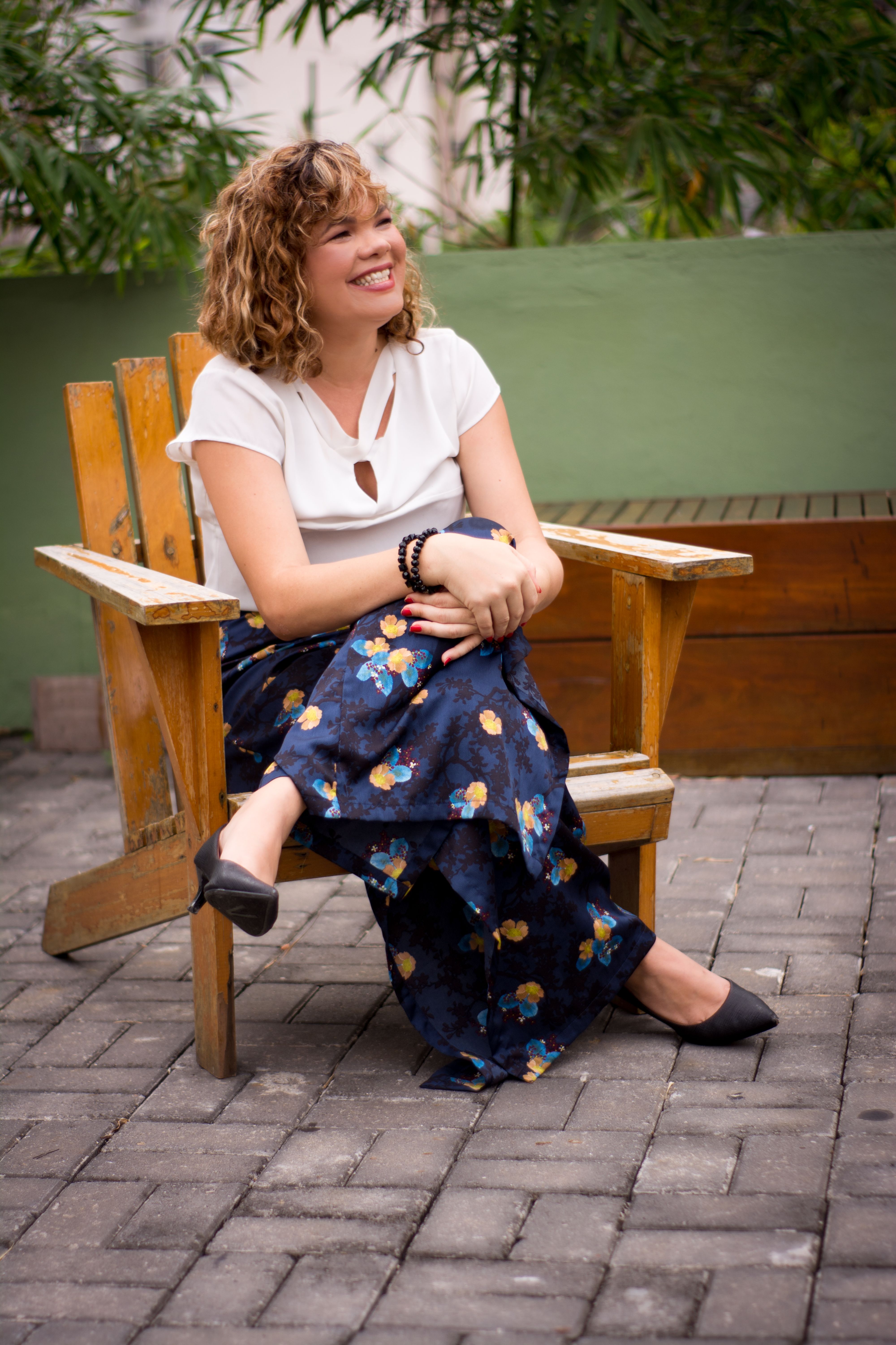 Fotomural Una mujer adulta alegre sentada en una silla de madera en un jardín, disfrutando de un día soleado.