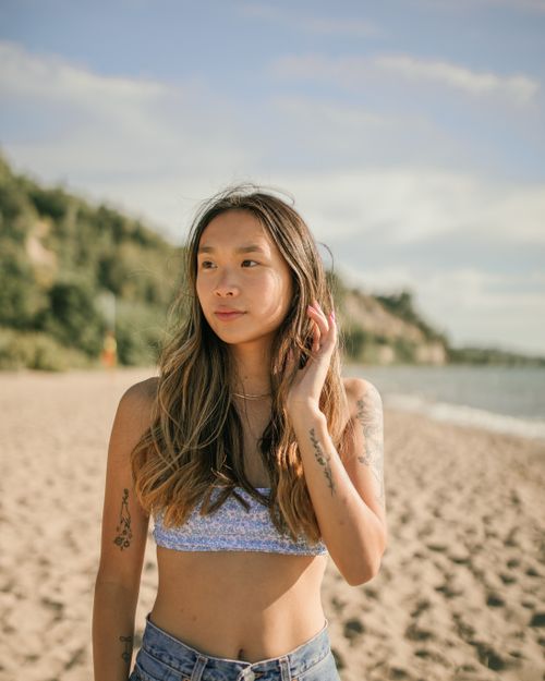 Free A tattooed Asian woman in a crop top enjoys a sunny day on the beach. Stock Photo