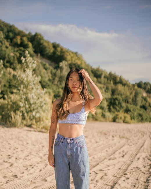 Woman in crop top and jeans poses on a sunny beach, exuding a summer vibe.