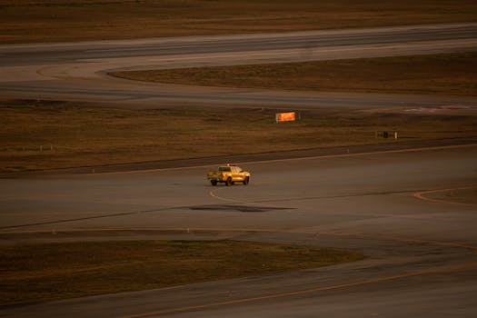 A yellow pickup truck drives across the open runway at Guarulhos International Airport.