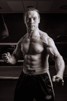 Powerful black and white portrait of a strong, shirtless boxer posing in a gym, showcasing defined muscles.