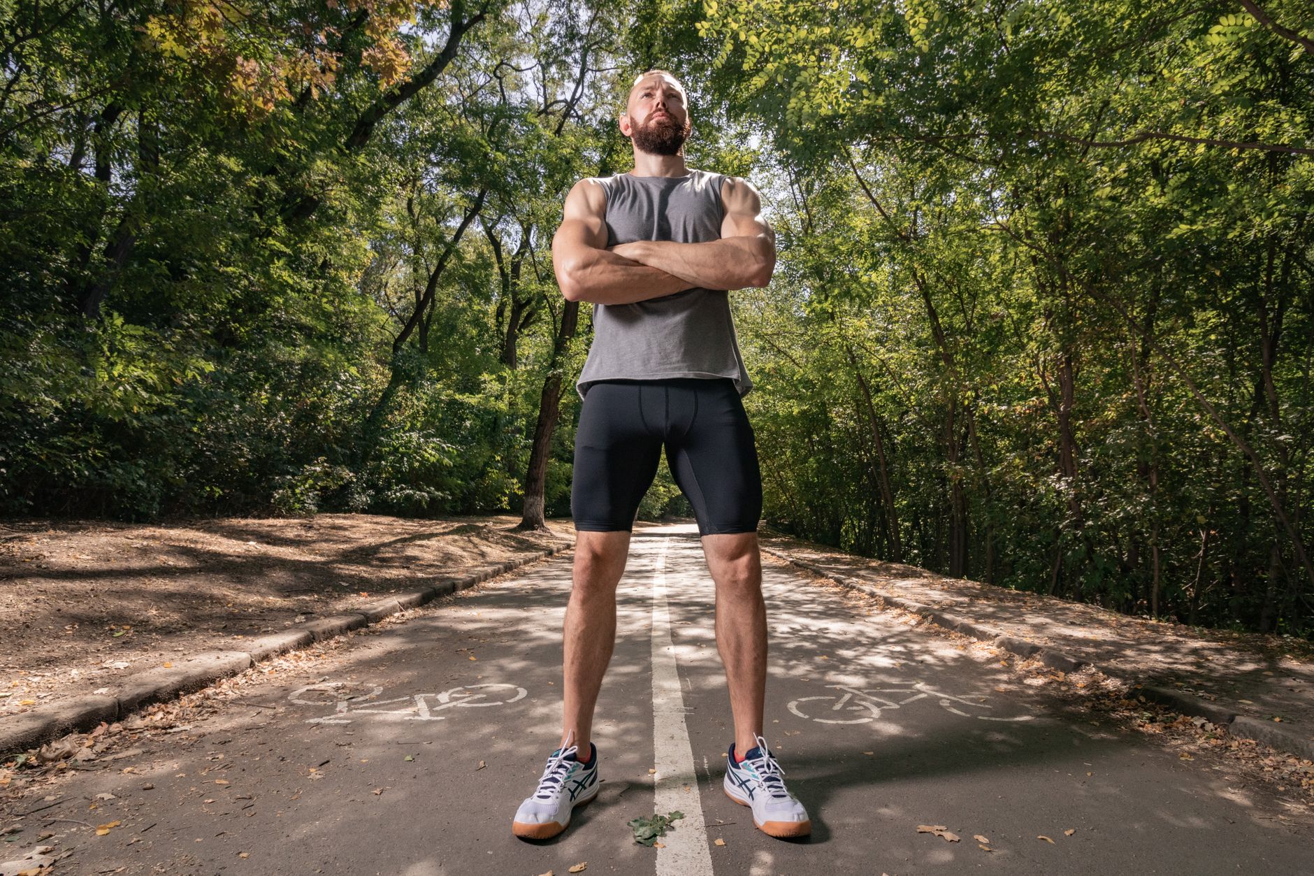 Athlete with arms crossed stands confidently on a forest path wearing sportswear.
