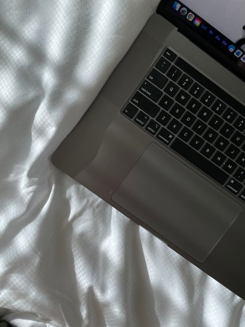 Free A sleek laptop on a white bed, evoking minimalism and modern style. Stock Photo