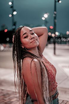Portrait of a smiling woman with long braided hair posing stylishly outdoors during the evening.