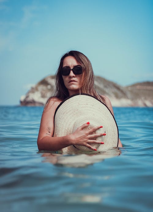 Free A Woman Wearing Sunglasses while Covering Her Body Using a Hat Stock Photo
