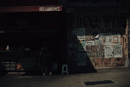 Moody urban street capture with graffiti and shadow contrasts by a snack stand.