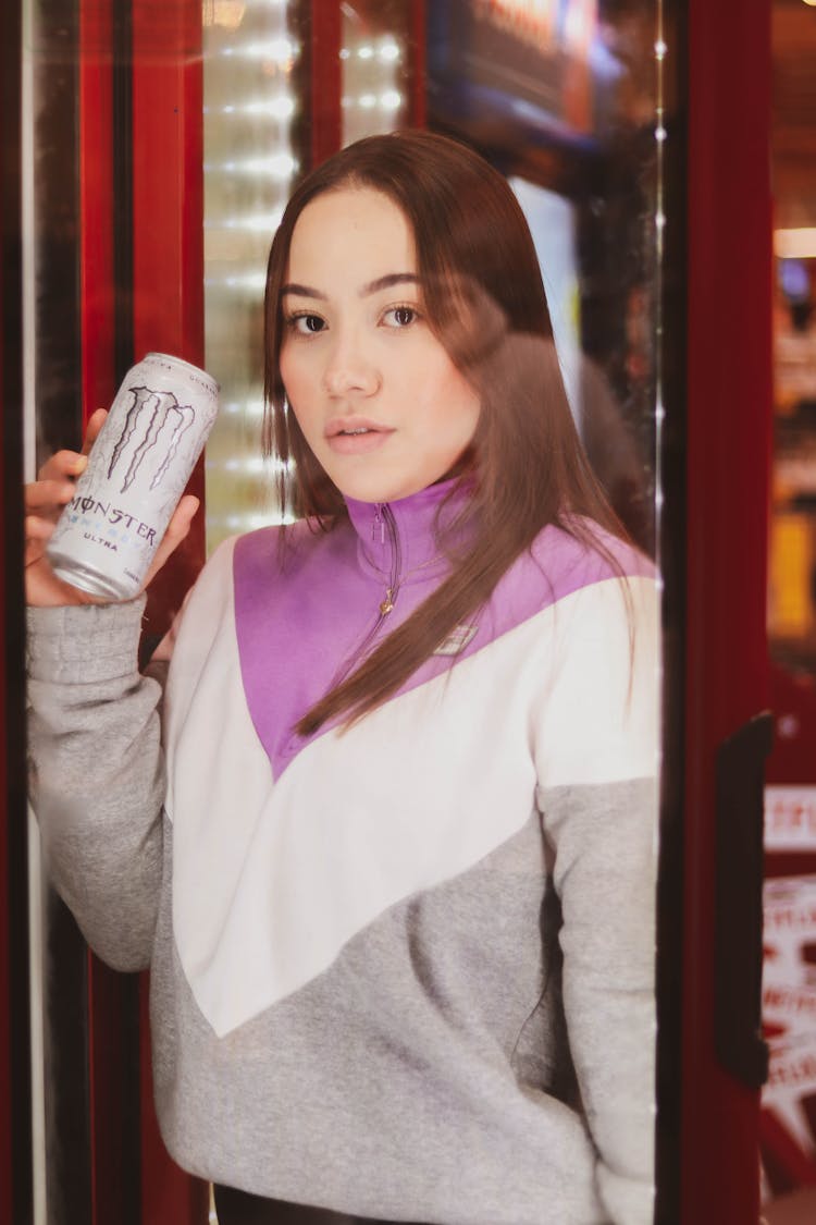 A Woman Holding A Canned Drink Behind The Glass