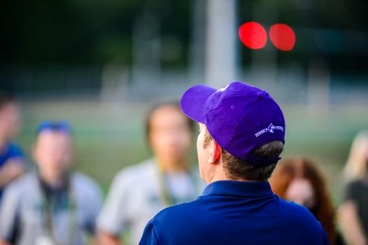 A man in a purple cap observing a group outdoors during the day.