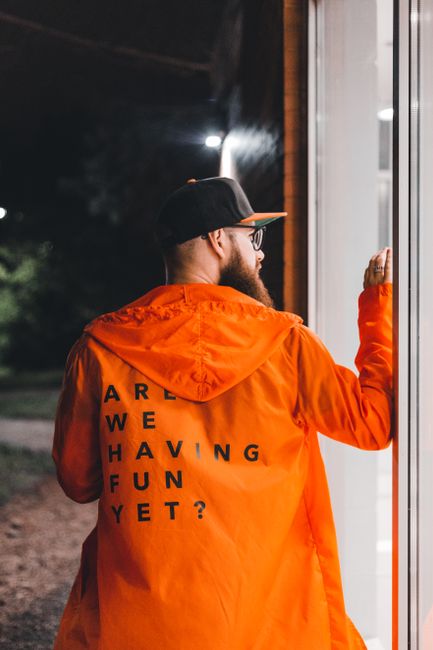 Man with beard and glasses wearing an orange jacket and cap, standing outdoors at night.