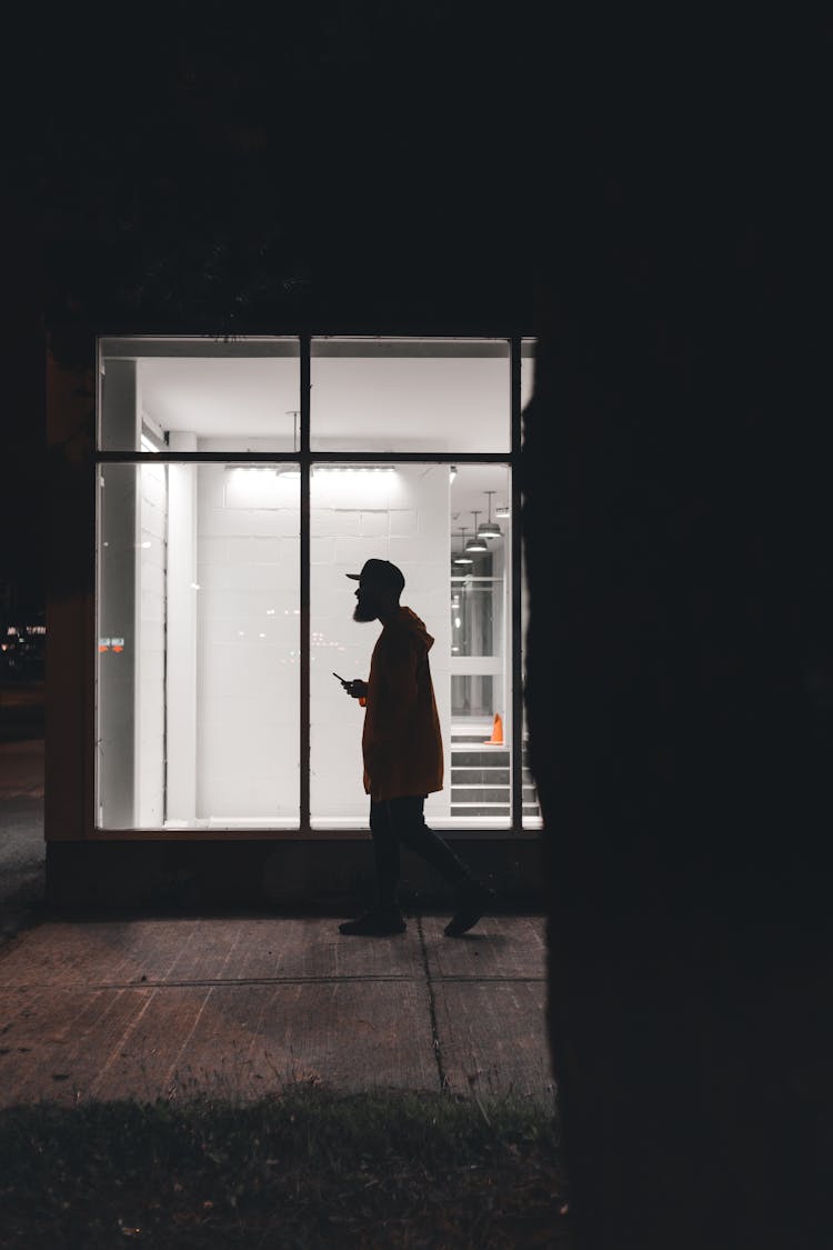 A Side View Of A Man Walking On The Street At Night