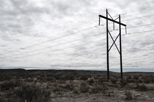 High voltage power lines stretch across a dramatic, cloudy sky landscape, embodying industrial beauty.