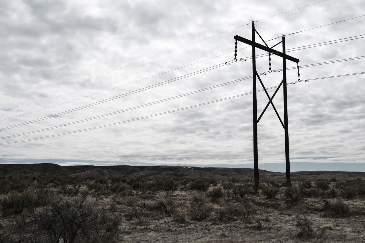 high voltage power lines stretch across a dramatic cloudy sky landscap