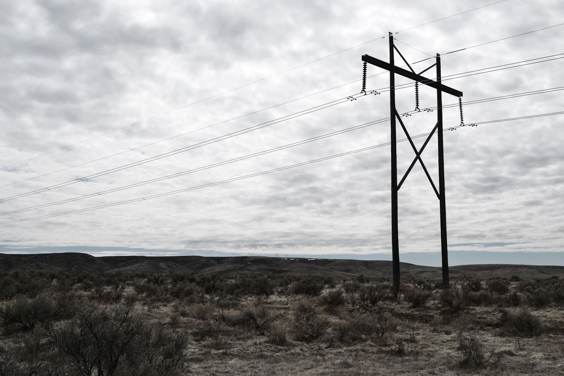 High voltage power lines stretch across a dramatic, cloudy sky landscape, embodying industrial beauty.