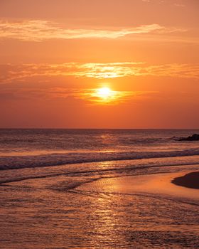 Orange sky and gentle waves create a serene beach sunset scene.