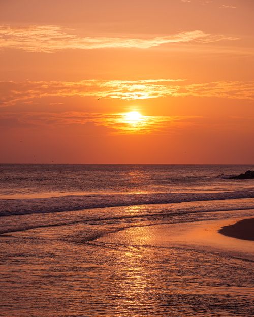 Free Orange sky and gentle waves create a serene beach sunset scene. Stock Photo