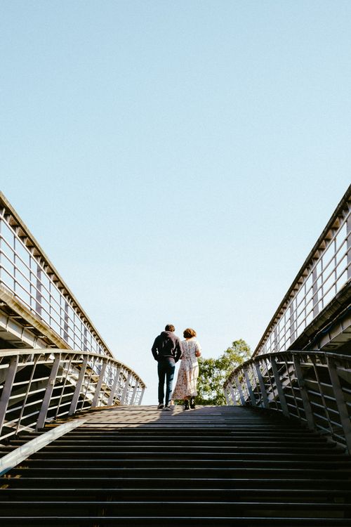 Free A couple walking upstairs on a modern urban bridge under a clear sky. Stock Photo