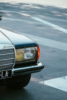Close-up of a vintage Mercedes Benz car parked on a city street corner with visible pavement and license plate.
