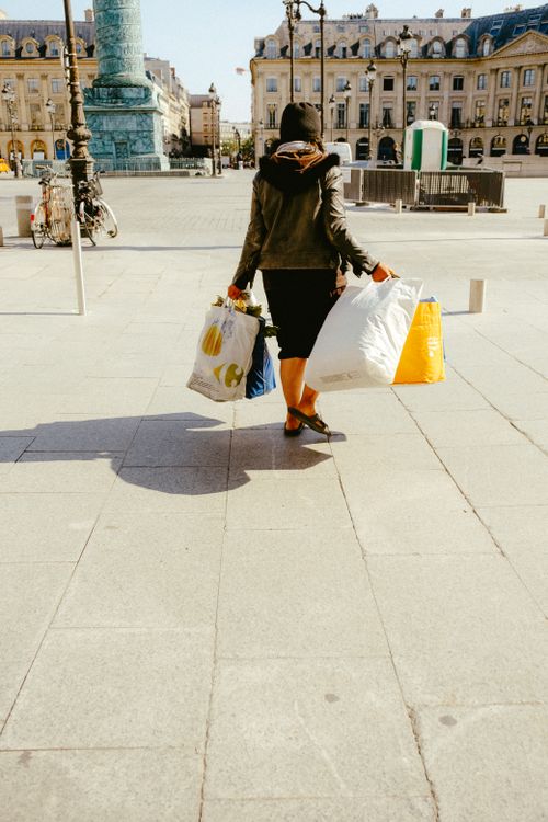 Free A woman walks in a city square carrying shopping bags, with a historic monument in the background. Stock Photo