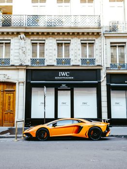 A sleek orange Lamborghini sports car parked in front of an elegant city building, exuding luxury and style.