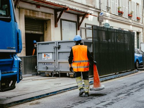 Free A construction worker in safety gear walks on a city street holding a traffic cone. Stock Photo