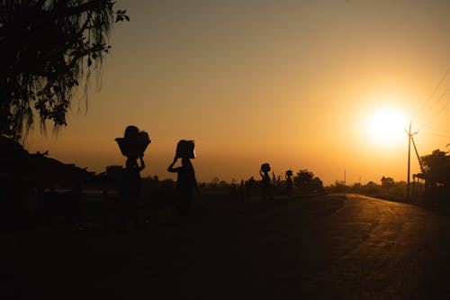 Silhouette of People Carrying Loads on Their Heads While Walking on the Road during Sunset