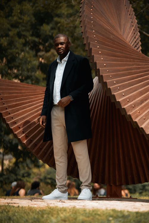 Free Elegant man in black coat poses by a modern sculpture in Ottawa's outdoors park. Stock Photo