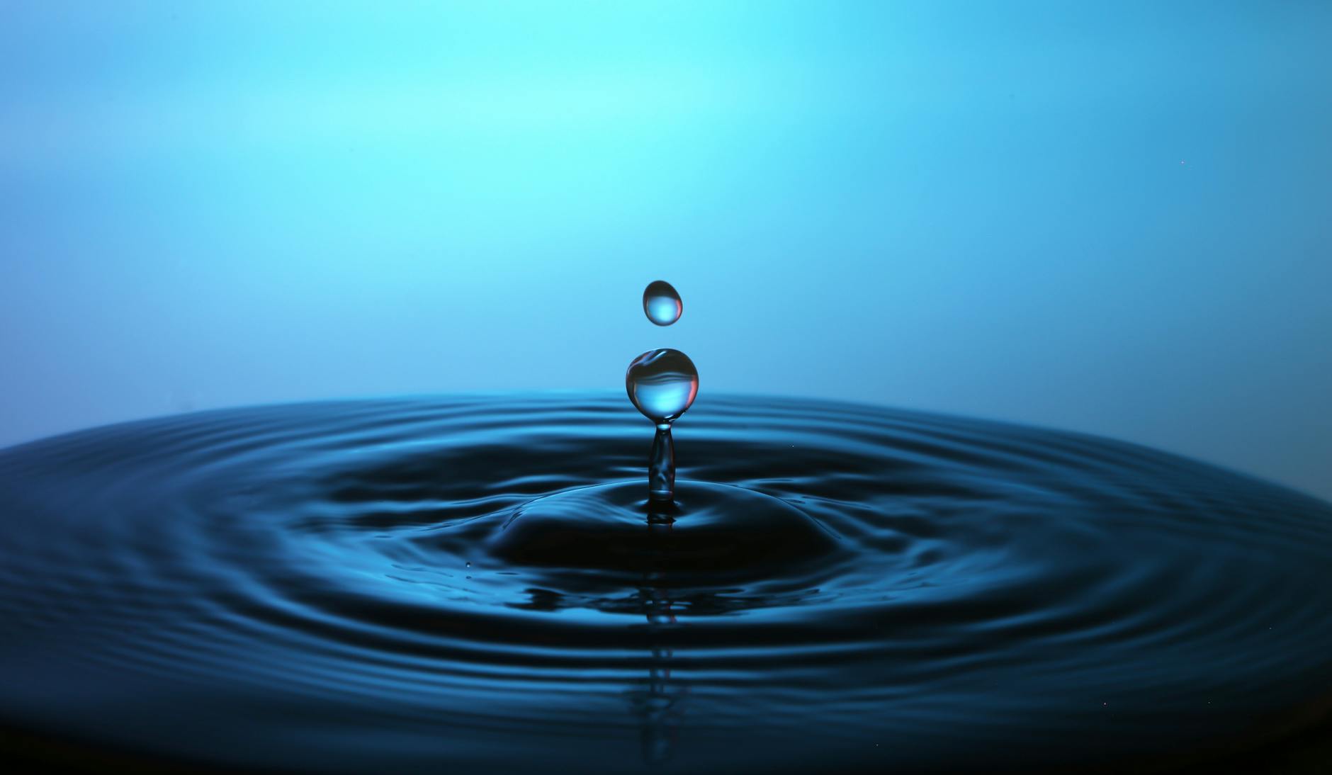 Macro shot of a perfect water droplet splash creating ripples on a blue background.