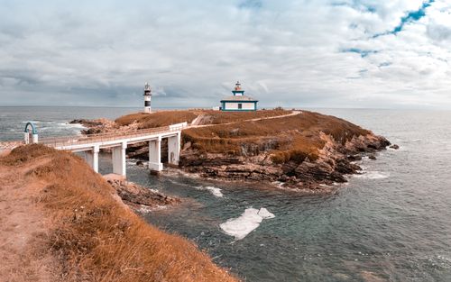 Free A captivating view of a coastal island with a lighthouse and bridge under a cloudy sky. Stock Photo