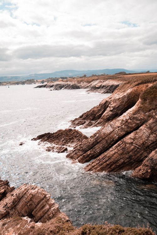 Free Dramatic cliffs along the seashore with waves crashing under a cloudy sky. Stock Photo