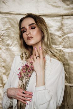Elegant woman posing with eyes closed, holding flowers against a silk backdrop.