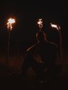 Silhouette of Man Sitting Near Burning Torches