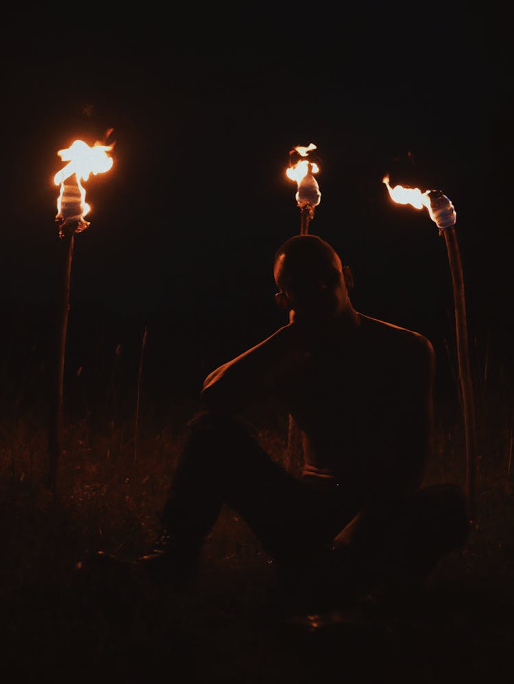 Silhouette Of Man Sitting Near Burning Torches