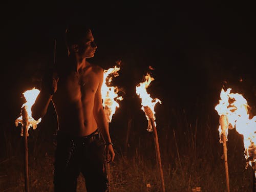 Topless Man Standing Near Burning Torches