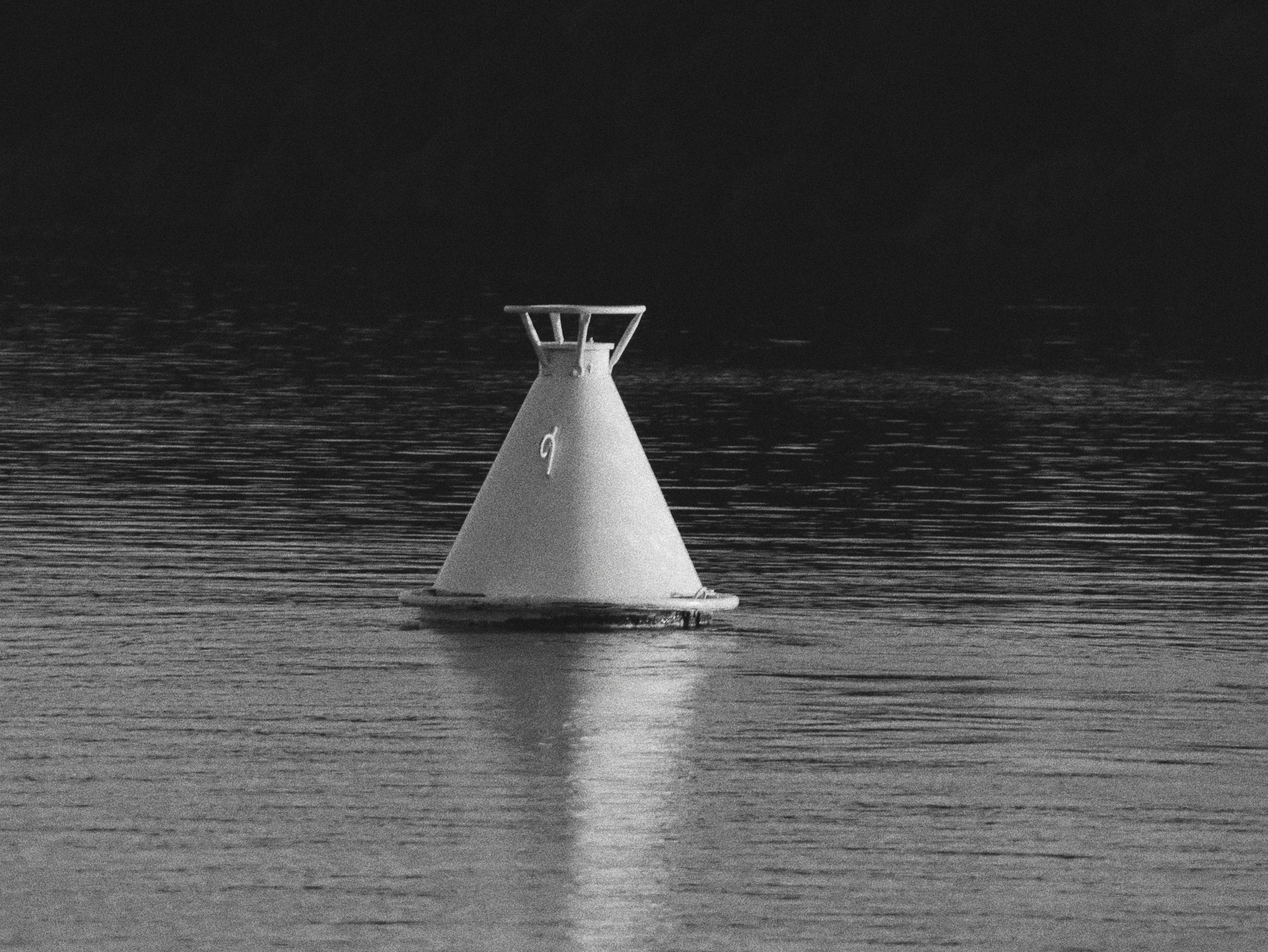 A black and white capture of a buoy floating on calm water.