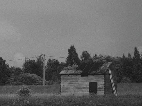 Black and White Picture of a Broken Wooden Shed on a Field 