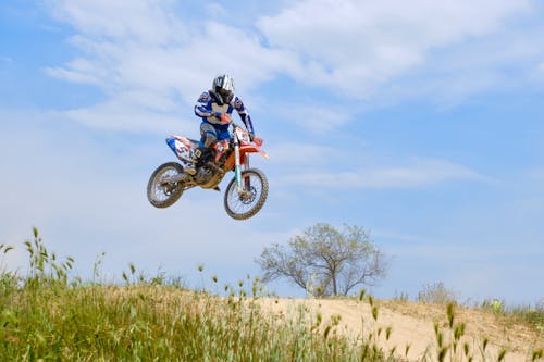 Free Man Riding Motocross Dirt Bike on Green Grass Field Under Blue and White Cloudy Sky during Stock Photo