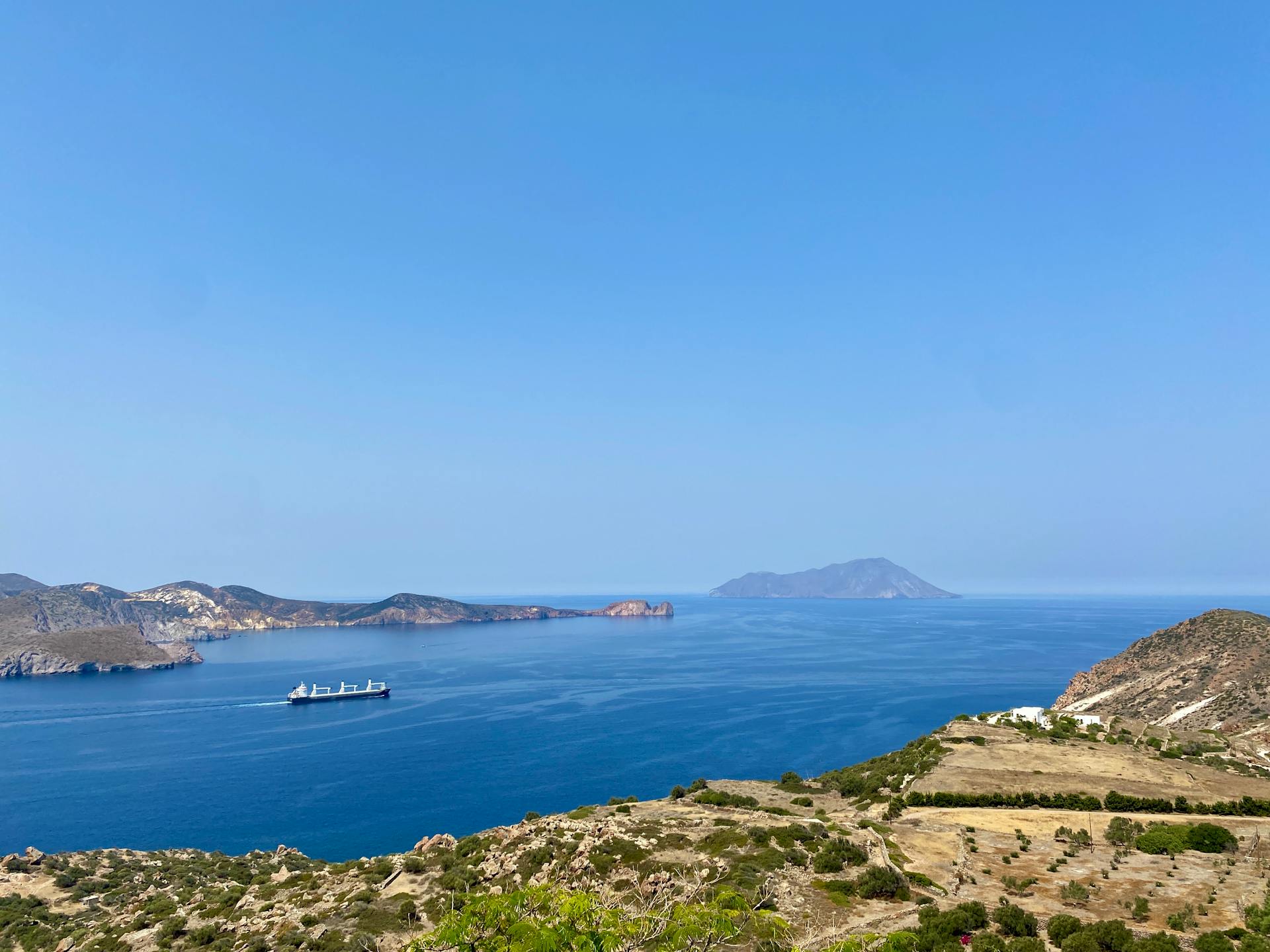 A stunning view of the Milos coastline with islands and a ship in the clear blue sea under a bright sky.