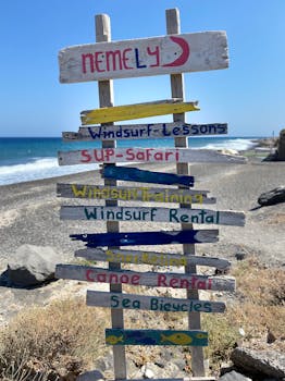 Vibrant wooden signs on a beach in Fira, Greece, offering various water activities.