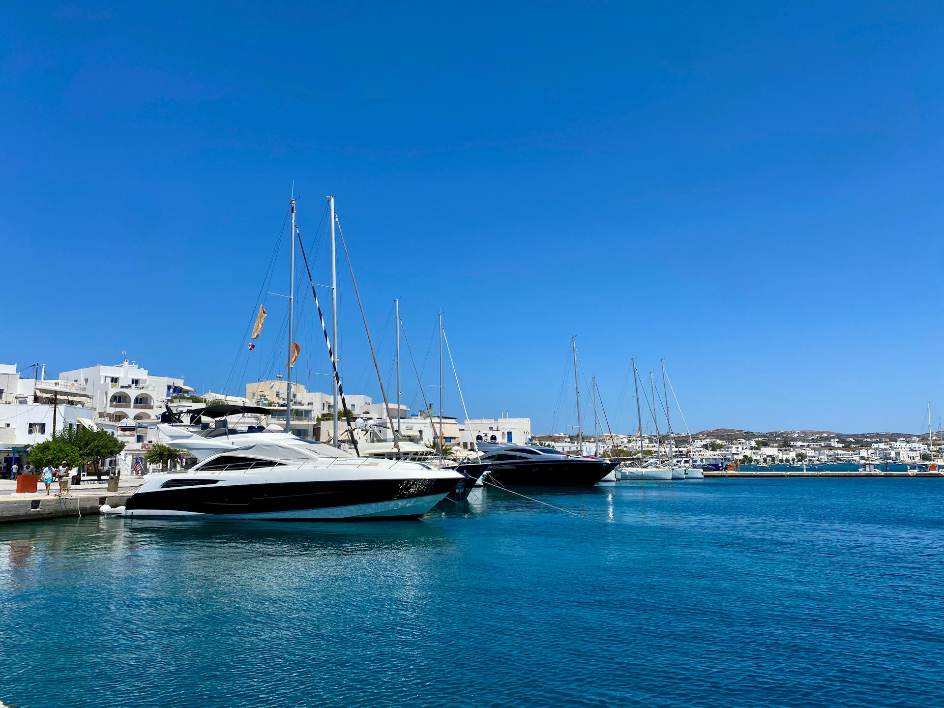 Scenic view of yachts at the Milos harbor with clear blue waters and a sunny sky.