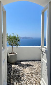 Open doors revealing a breathtaking view of the Aegean Sea from a Fira balcony.