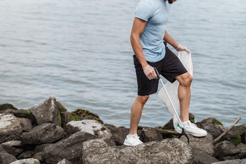 Man in Blue T-shirt and Black Shorts Standing on Rock Near Body of Water during