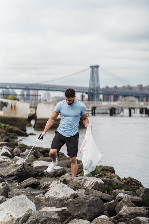 Man in White T-shirt and Brown Shorts Standing on Rock Near Body of Water during