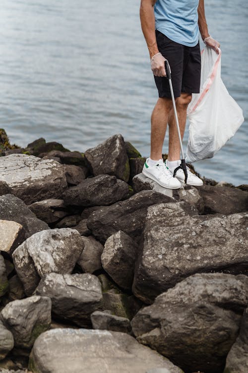 Free Person in Black Shorts and White Sneakers Standing on Rocky Shore Stock Photo