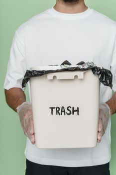 Man holding a trashcan, emphasizing recycling and waste management indoors.
